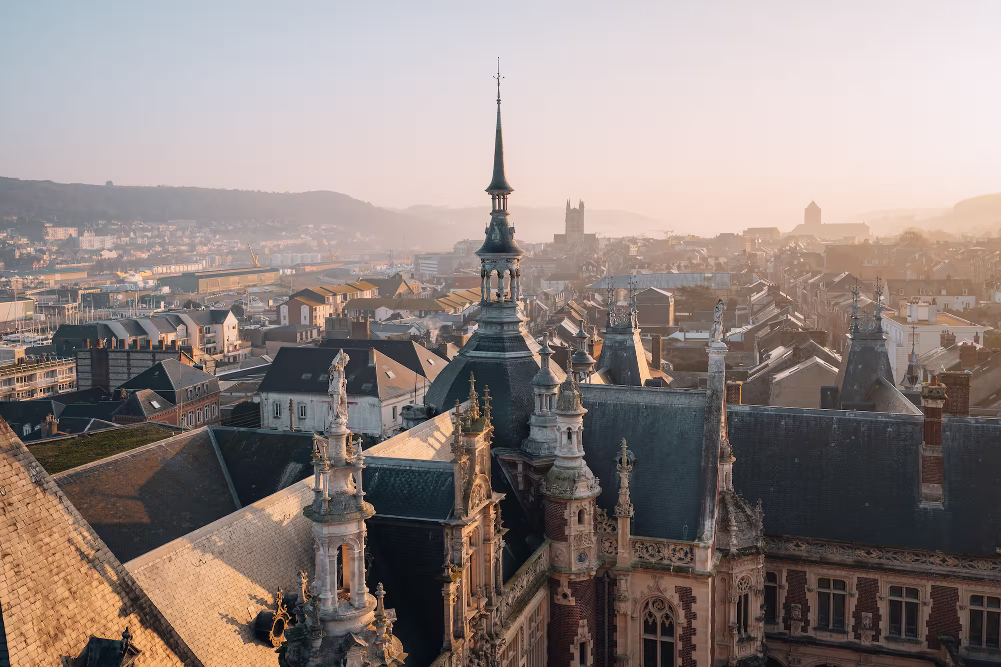 Bâtiment historique avec architecture ornée, flèches et détails en pierre, sur fond d'une ville au coucher de soleil.